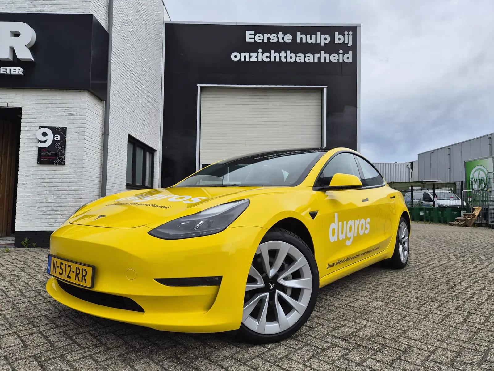 Low front-quarter view of the yellow-wrapped Tesla with Dugros logos on the bonnet and door.