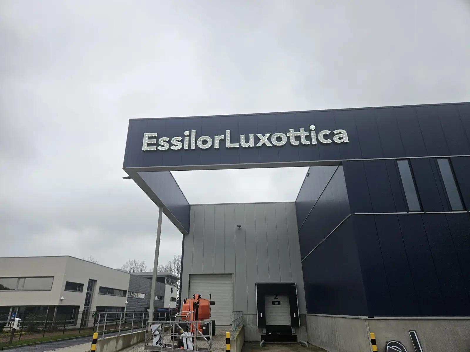 Montagebeeld van de EssilorLuxottica-letters boven de entree met hoogwerker.