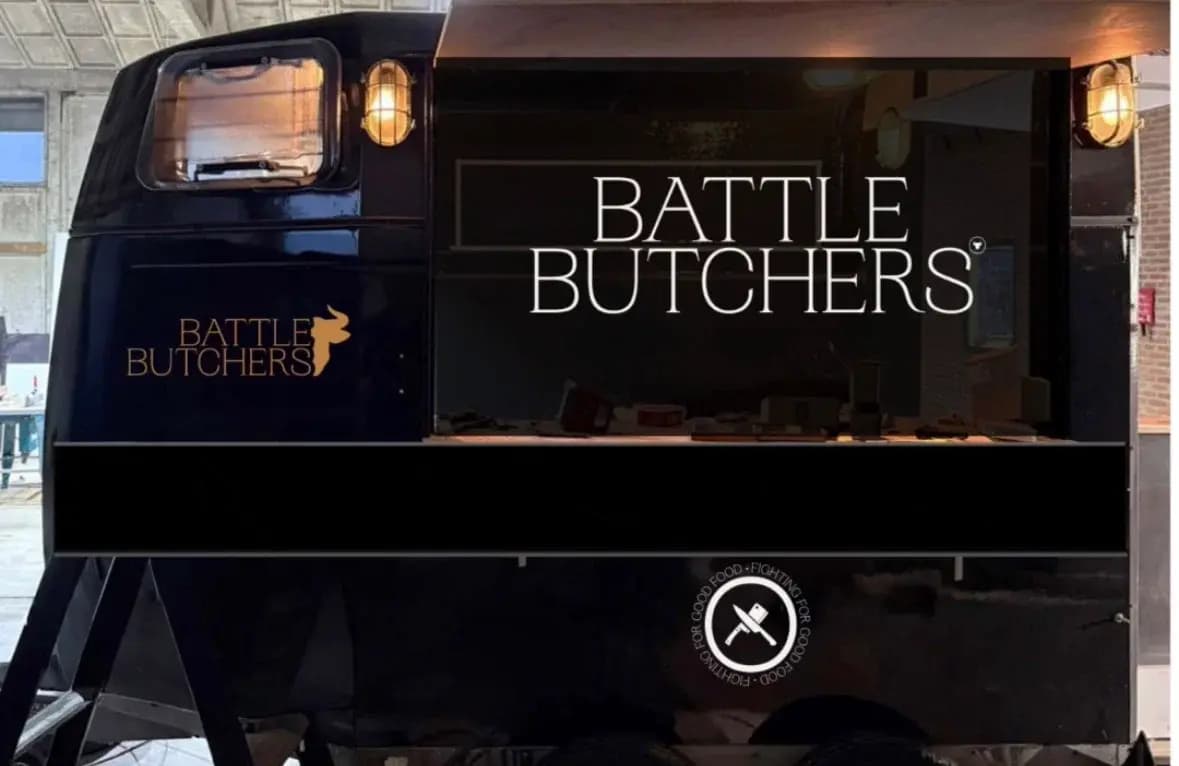 Battle Butchers foodtruck met donkere buitenzijde, gouden logo en geopende verkoopklep.