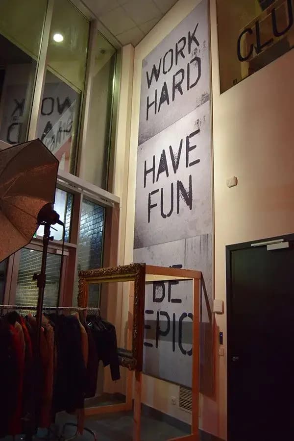 Grote verticale muurprint met motiverende typografie “WORK HARD HAVE FUN” op een hoge binnenwand, geplaatst in een modern interieur met industriële uitstraling.