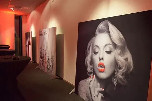 Gang met sfeerverlichting en vrijstaande grootformaat fotopanelen, waaronder een zwart-wit portret van een vrouw met rode lippen, opgesteld in een modern eventinterieur.