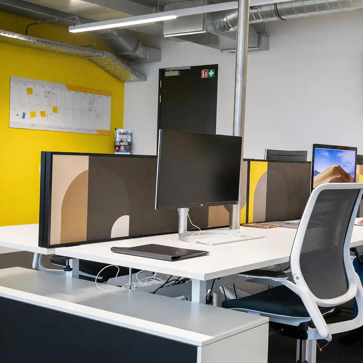 Kantoorinterieur met bedrukte bureaupanelen, gele accentwand en werkplekken, toegepast als decoratieve interieurbelettering en functionele privacy signing.