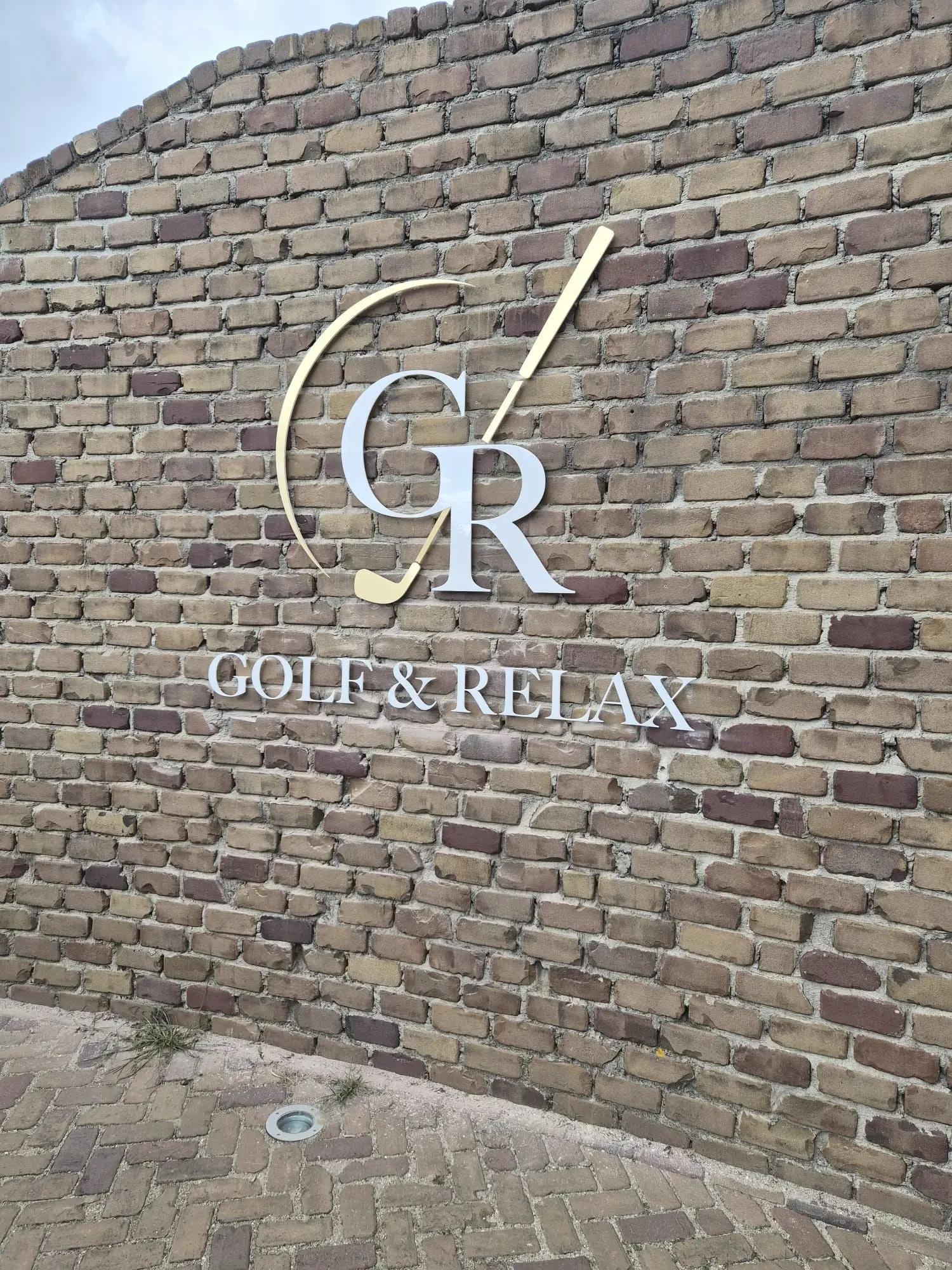Losse witte en goudkleurige Golf & Relax-letters op de bakstenen gevel.