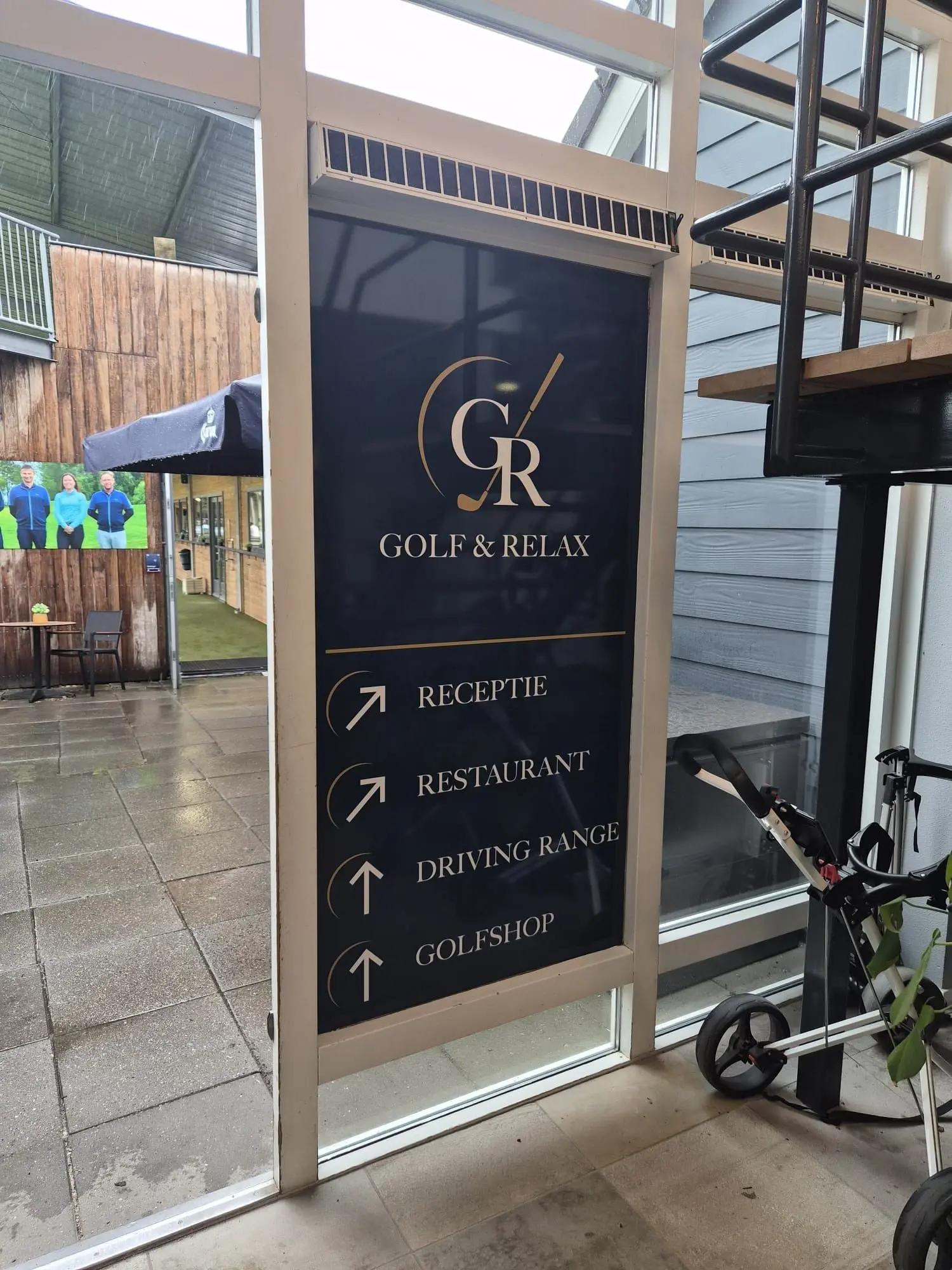 Bewegwijzering op glas aan de binnenzijde, met onder meer drivingrange en golfshop.