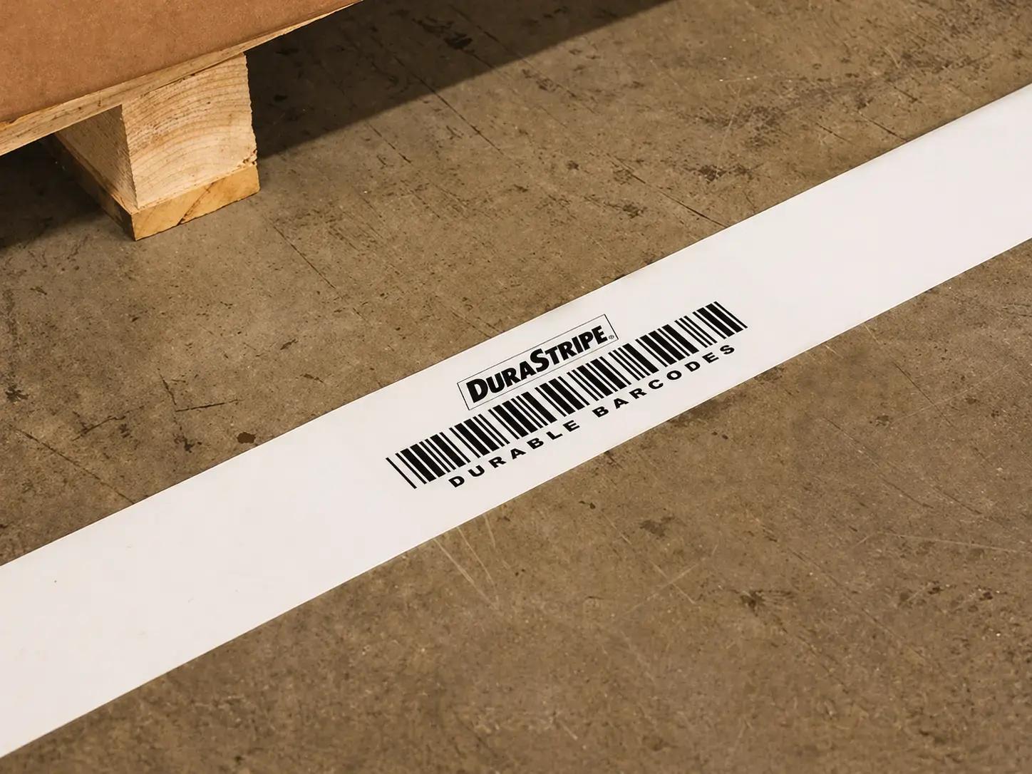 Witte DuraStripe vloermarkering met barcode op een industriële betonvloer, toegepast als duurzame identificatiesticker voor logistiek en magazijnbeheer.