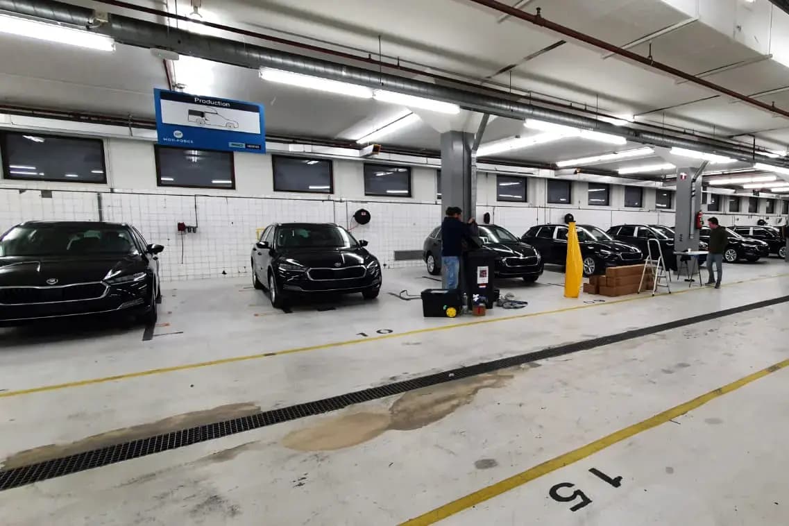 Werkplaats met meerdere zwarte auto’s in een productieruimte, waar monteurs bezig zijn met voertuigbelettering en voorbereiding van autoreclame.