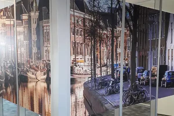Glazen scheidingswand in kantoor met full-colour glasfolie van een stadsgezicht met grachtenpanden en fietsen, toegepast als decoratieve privacyfolie.