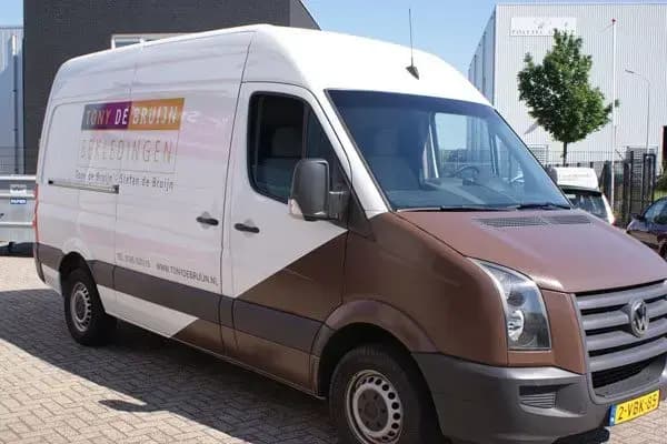 Witte bestelbus met bruine gedeeltelijke carwrap en voertuigbelettering op het zijpaneel, geparkeerd op een bedrijventerrein.