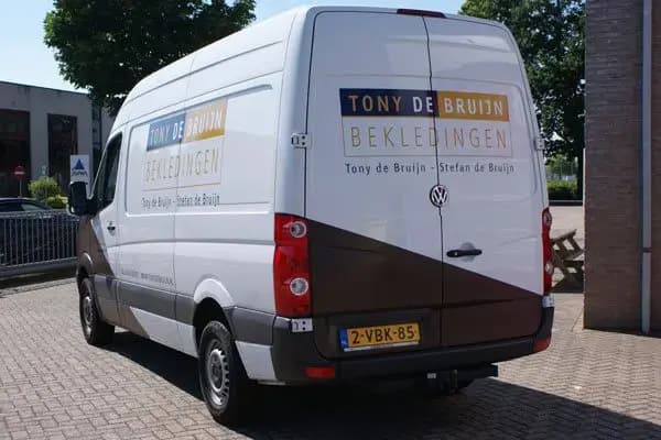 Achterzijde van een witte bestelbus met voertuigbelettering voor Tony de Bruijn Bekledingen en bruine geometrische carwrap op de zij- en achterpanelen, geparkeerd op een bedrijventerrein.
