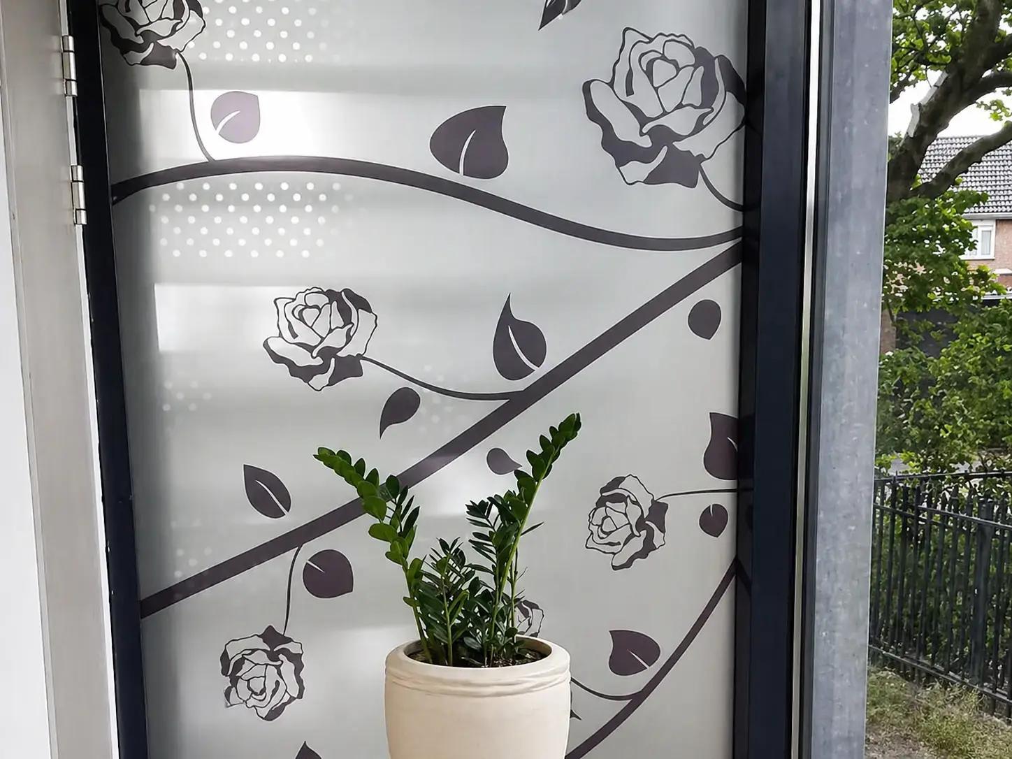 Matte glasfolie met bloem- en rankmotief op een raam, toegepast als decoratieve privacyfolie in een interieur met plantenbak.