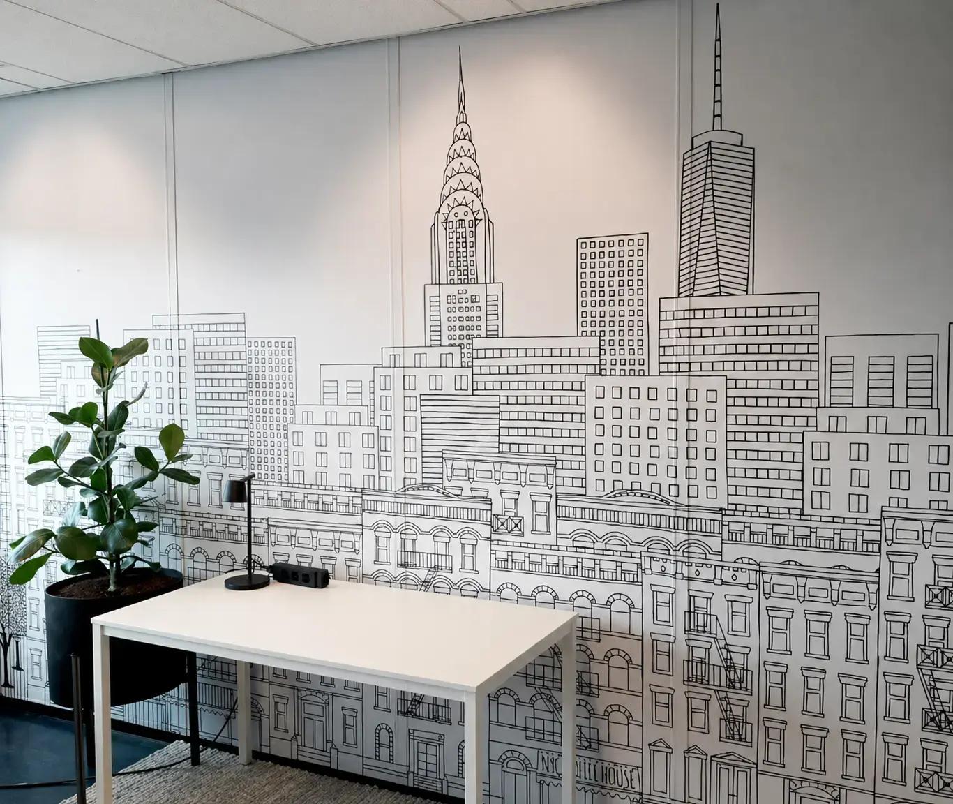 Kantoorruimte met kamerbrede wandprint van een zwart-witte stadsillustratie, toegepast als decoratieve muurvisual en interieurbelettering achter een werkplek.