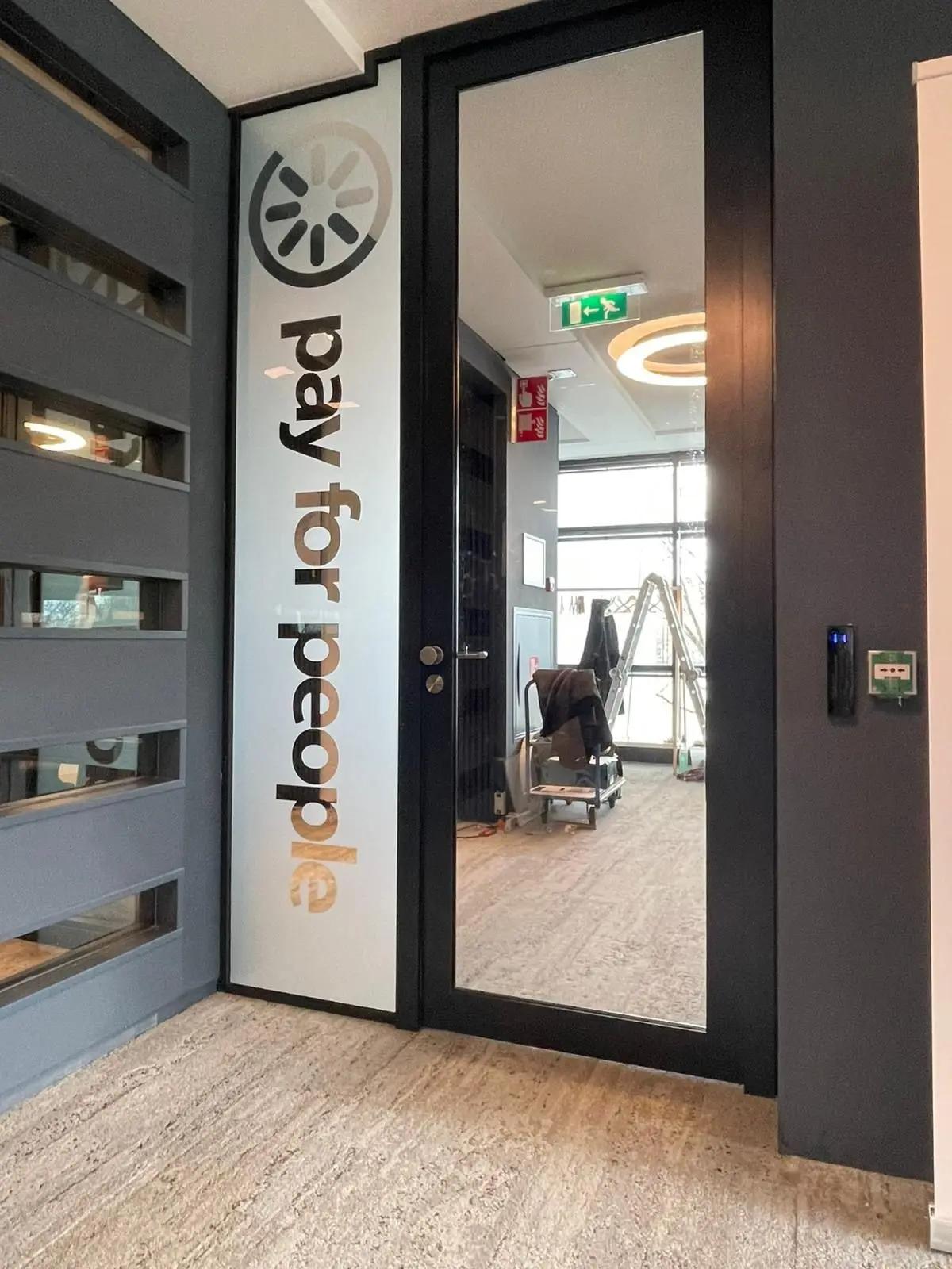 PayforPeople-logo en verticale belettering op een glazen deur in het kantoor.
