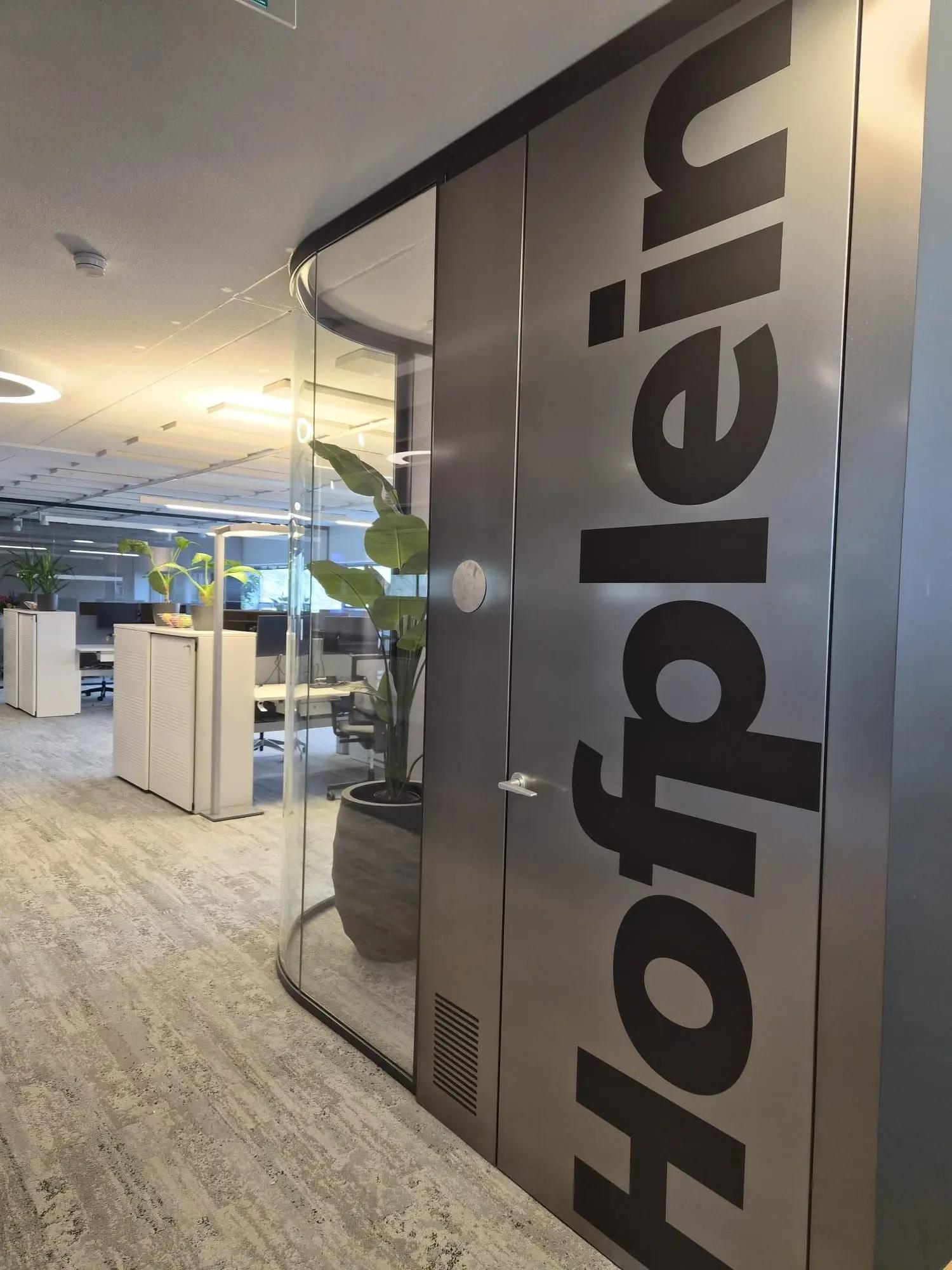 Grote verticale ruimtenaam Hofplein op een grijze wand naast de kantoorruimte.