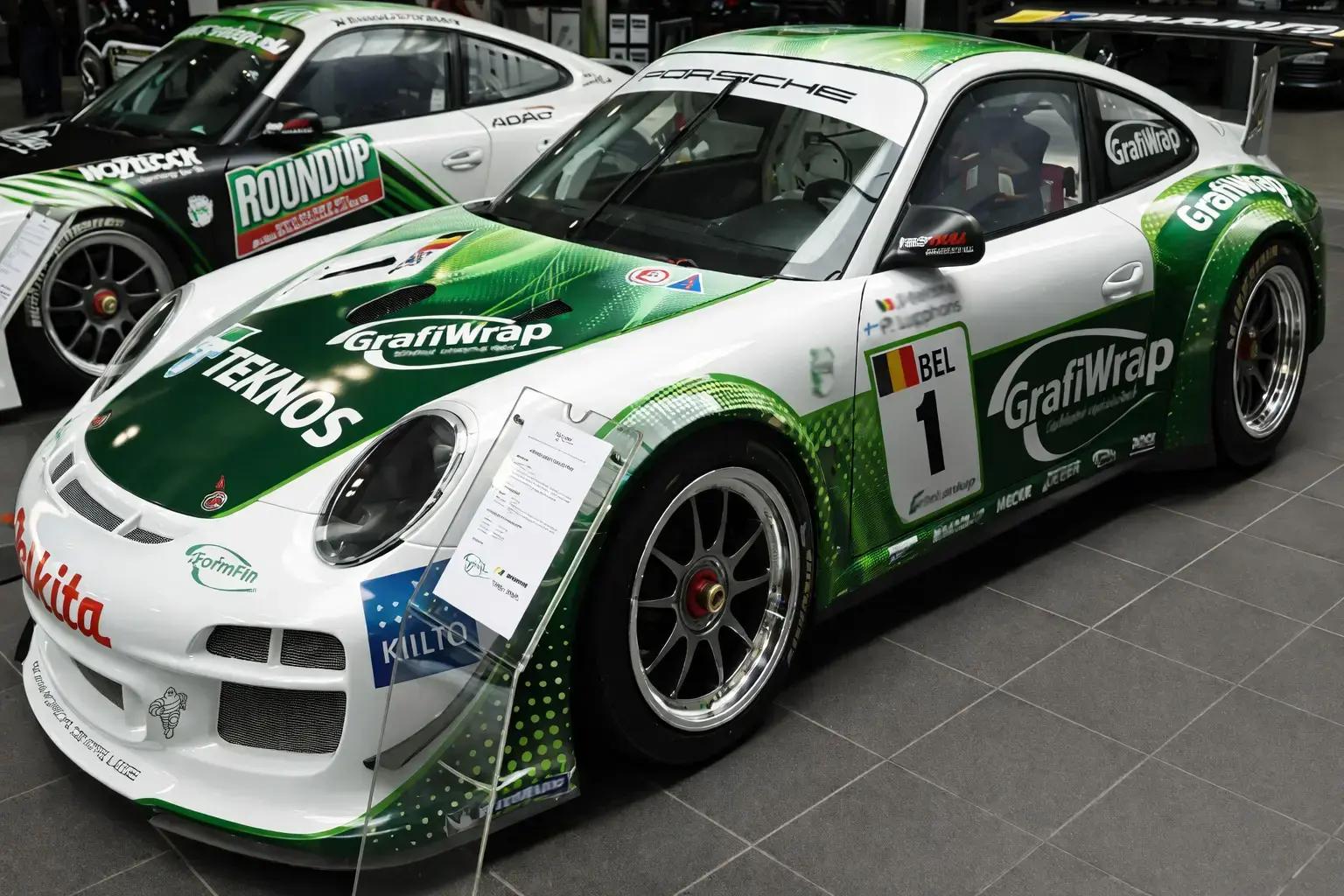 Wit-groene raceauto met volledige voertuigwrap, sponsorbelettering en grote logo’s op motorkap, deuren en spatborden, tentoongesteld in een showroom.