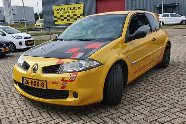 Gele personenauto met sportieve voertuigbelettering, zwarte motorkap en rode striping op de voorzijde en zijkant, geparkeerd op een bedrijventerrein.