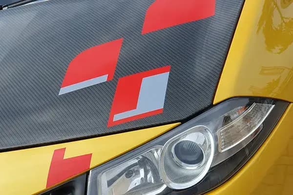 Close-up van een gele personenauto met carbonlook motorkap, rode grafische striping en koplampdetail als sportieve voertuigbelettering.