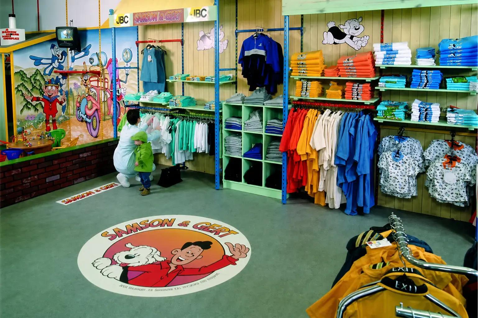 Kinderkledingwinkel met kleurrijke Samson & Gert wanddecoratie, schapbordjes, vloersticker en thematische signing voor een speelse winkelinrichting.