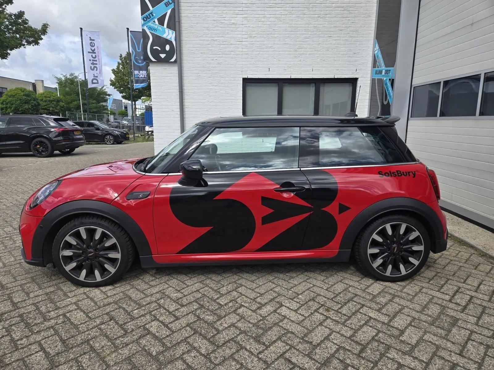 Rode Mini Cooper van Solsbury van opzij, met grote zwarte folievormen over de portieren.