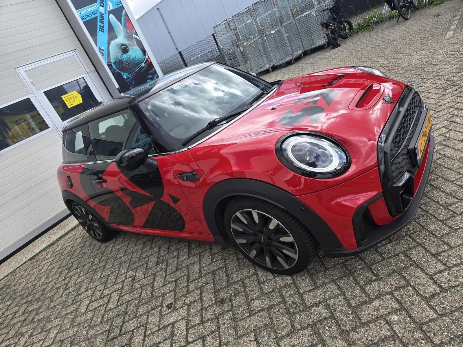 Mini Cooper met zwarte belettering op motorkap en zijkant, van schuin voor gezien.