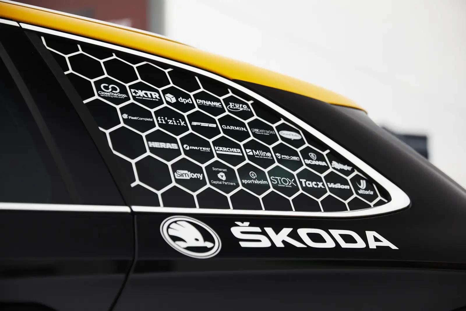 Zwarte en gele Škoda met sponsorbelettering op de zijruit, voorzien van witte honingraatprint, diverse logo’s en Škoda-voertuigreclame op de carrosserie.