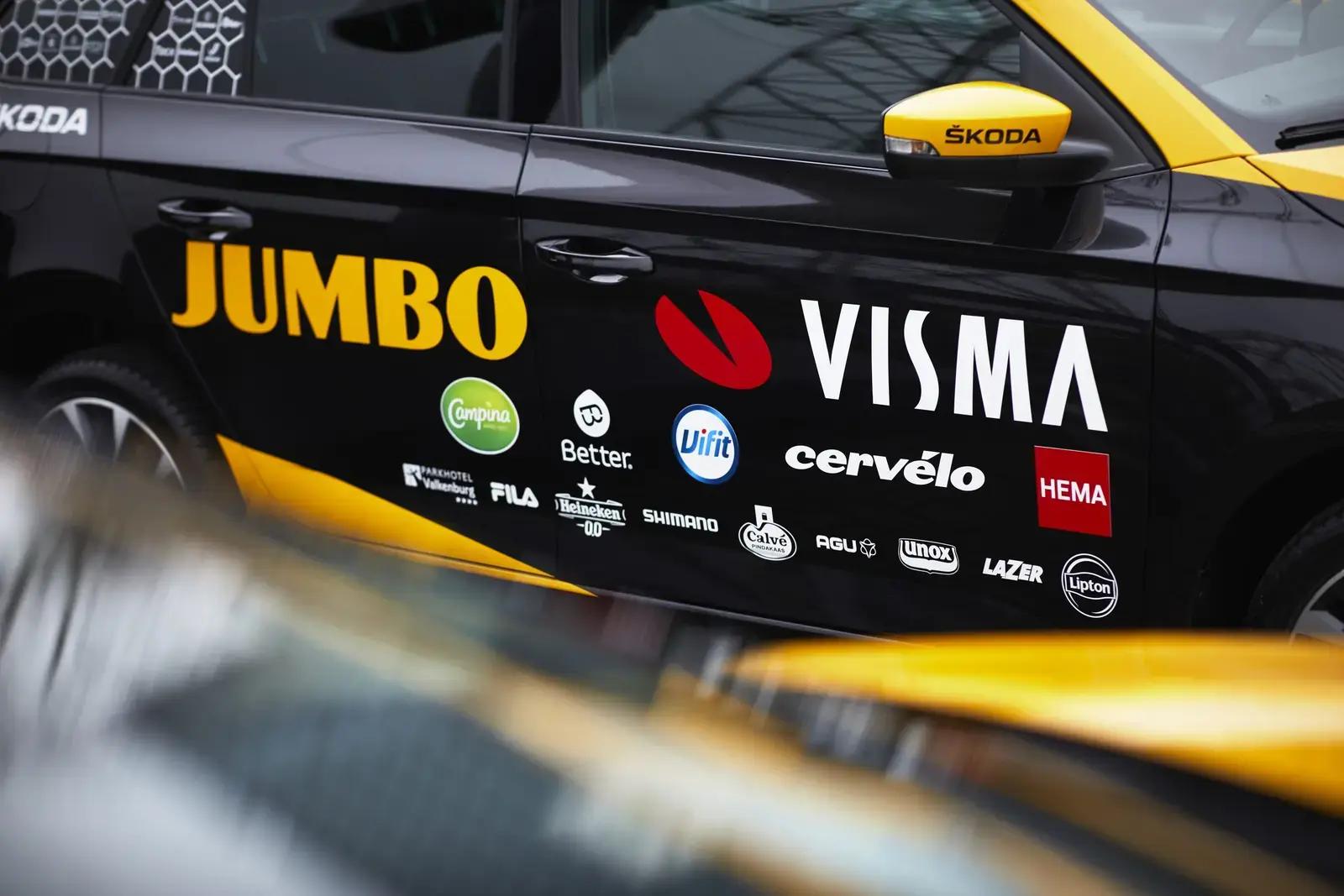 Zwarte Škoda met gele accenten en voertuigbelettering van Jumbo Visma op de portieren, voorzien van meerdere sponsorlogo’s als full-colour autoreclame.