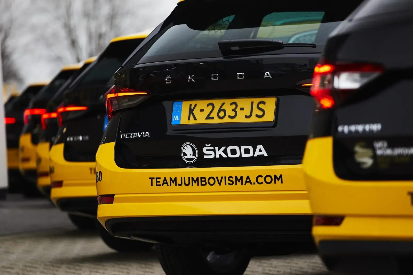 Rij zwarte en gele Škoda-teamauto’s met voertuigbelettering op de achterzijde, voorzien van Škoda-logo en websitebedrukking "teamjumbovisma.com" op de bumper.