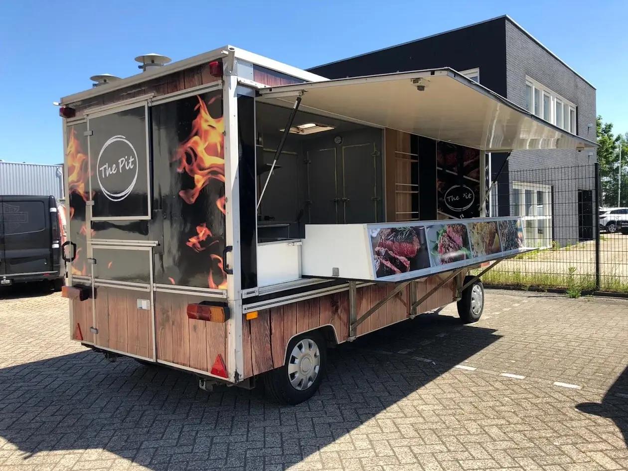 The Pit catering trailer with an open serving hatch, flame graphics, a wood-effect print and food photographs.