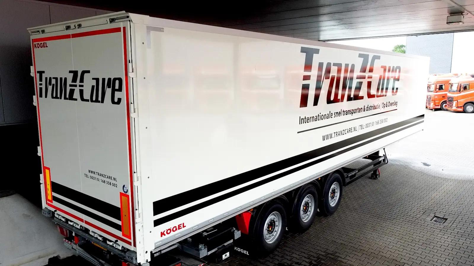 White Kögel trailer with large Tranzcare logos and black lines