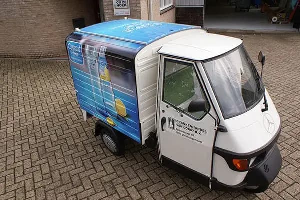 Compacte bezorgscooter met gesloten laadbak en full-color voertuigbelettering voor Crystal Clear, voorzien van productafbeeldingen op de zijpanelen en bedrijfslogo op het portier.