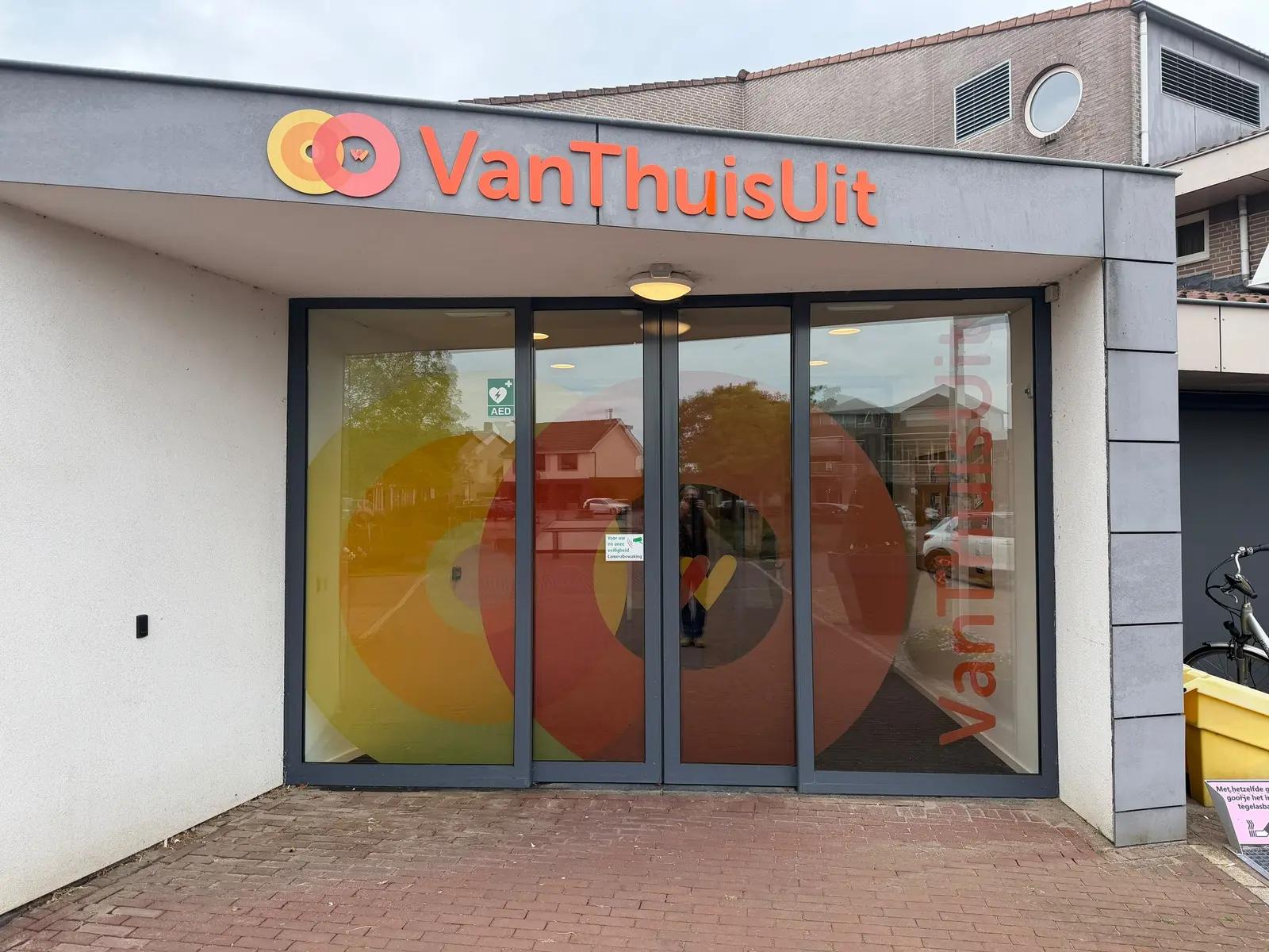 Entree van VanThuisUit met oranje acrylaatletters en gekleurde cirkels op de glazen deuren.