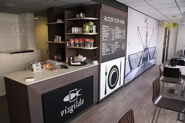 Interieur van een viswinkel of lunchruimte met houten toonbank, Visgilde-baliebelettering, menubord en grote wandprint van een vissersboot.