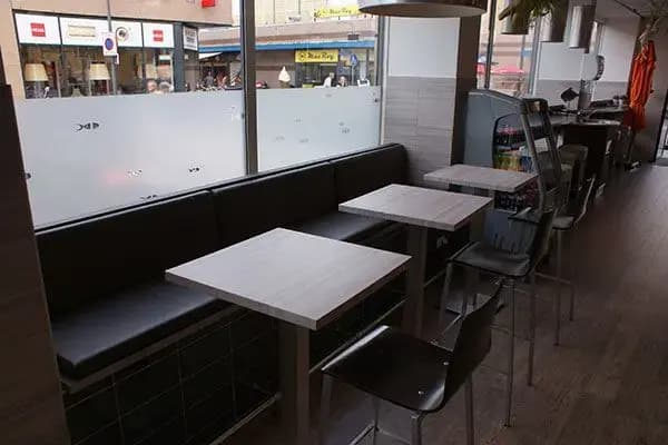 Zitgedeelte van een viswinkel met tafels langs de glazen pui, voorzien van matte raamfolie met subtiele visiconen voor privacy en interieurbeleving.