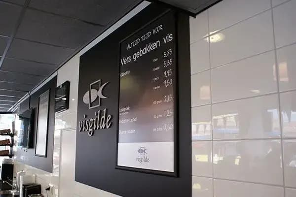 Zwarte wandpanelen met Visgilde-logo en menubord voor gebakken vis, gemonteerd op een wit betegelde winkelwand in een moderne viszaak.