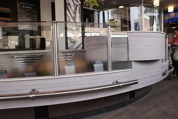Gebogen verkoopbalie in een viswinkel met glazen spatscherm, houten frontpanelen en RVS leuning, geplaatst in een modern winkelinterieur.