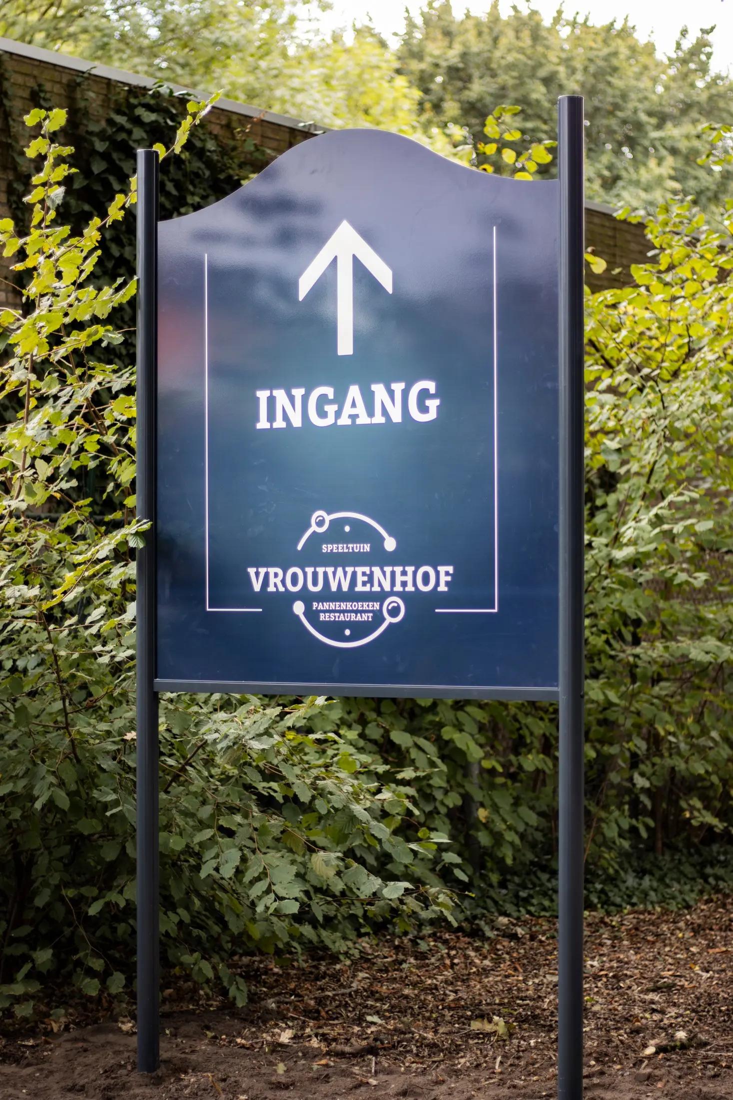 Vrijstaand ingangsbord van Vrouwenhof met witte pijl en logo