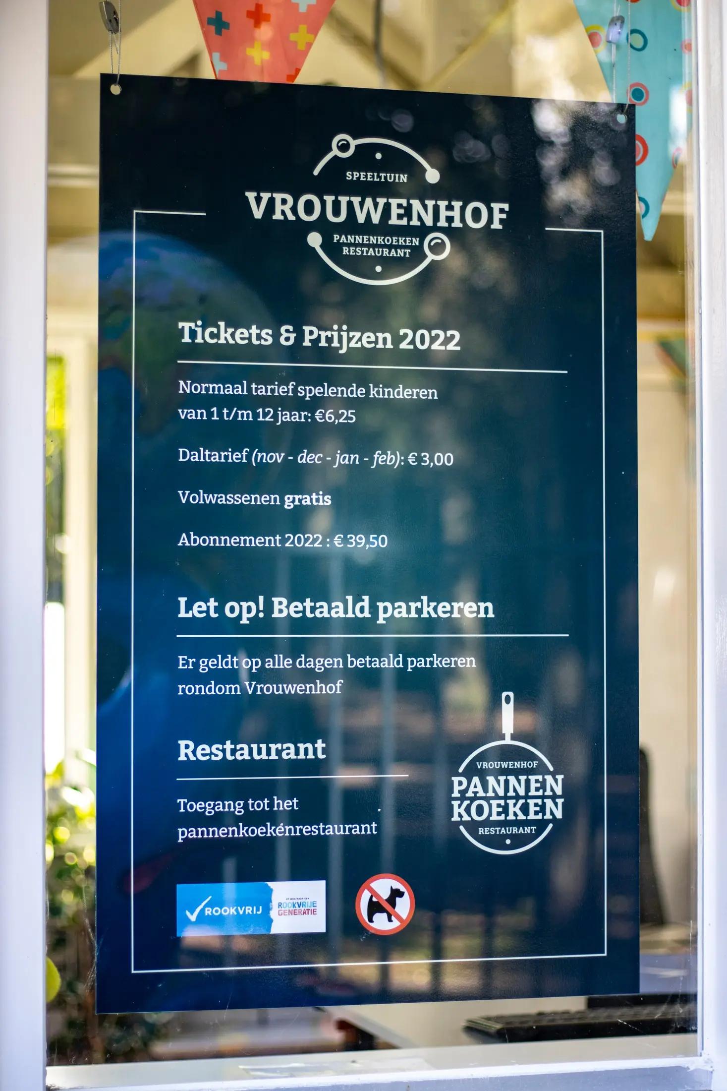 Detail van het Vrouwenhof-logo en bezoekersinformatie op glas