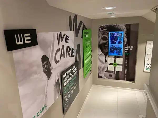 Trappenhuis met grote wandvisuals en interieurbelettering met de slogan "WE CARE", gecombineerd met fotopanelen en informatieve muurcommunicatie in een moderne kantooromgeving.