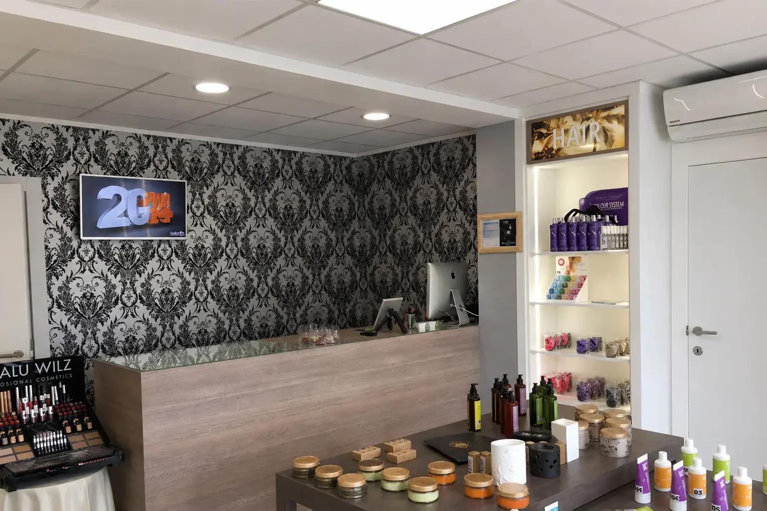 Kapsaloninterieur met verlichte HAIR-signing boven een productdisplay, decoratief wandpatroon en presentatieruimte voor professionele haarproducten.
