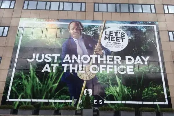 Kantoorgevel met groot full-color geveldoek over meerdere verdiepingen, voorzien van een campagnebeeld en witte typografie met de teksten “Just another day at the office” en “Let’s meet”.