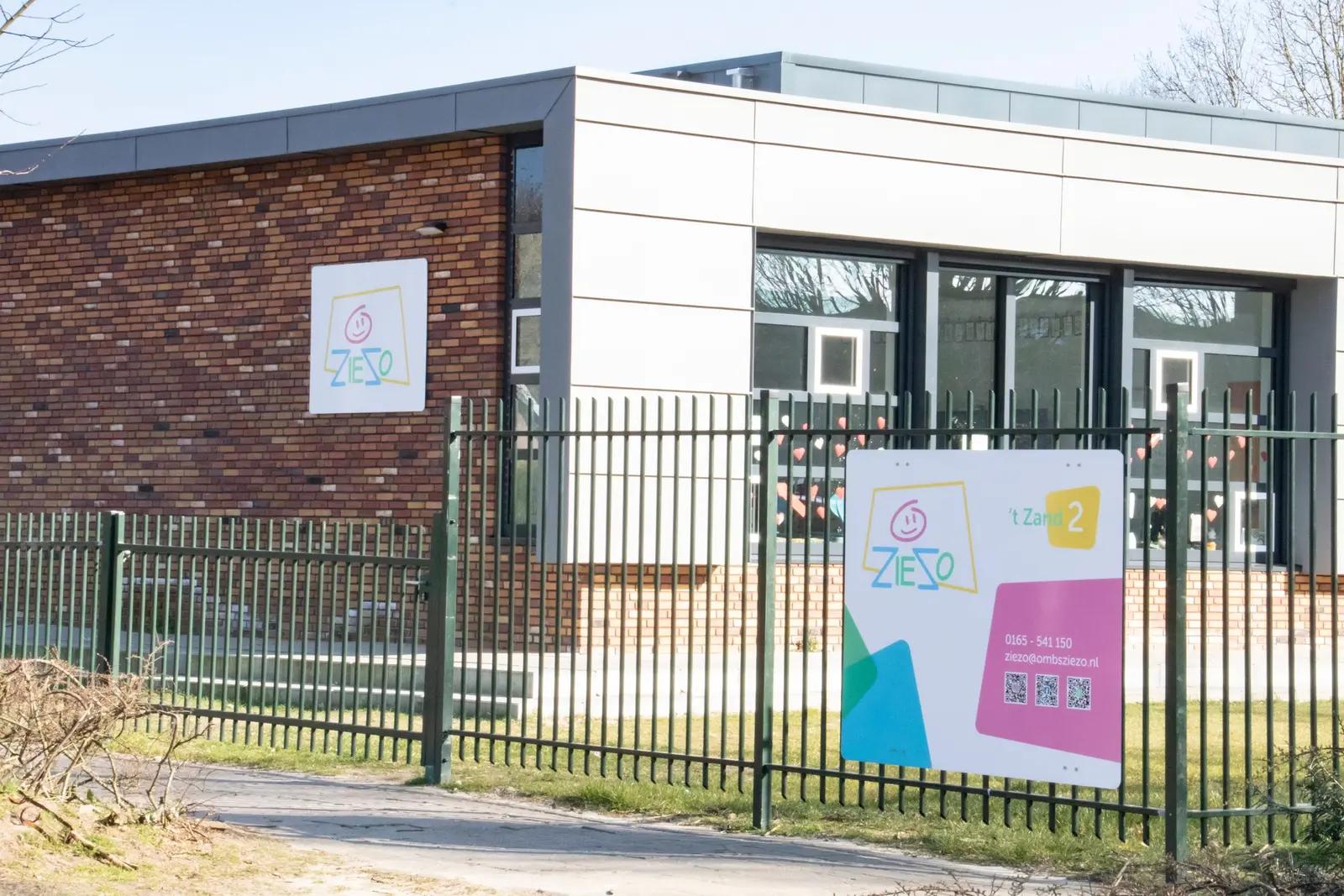 Schoolgebouw met gevelbord en informatiebord bij het hek