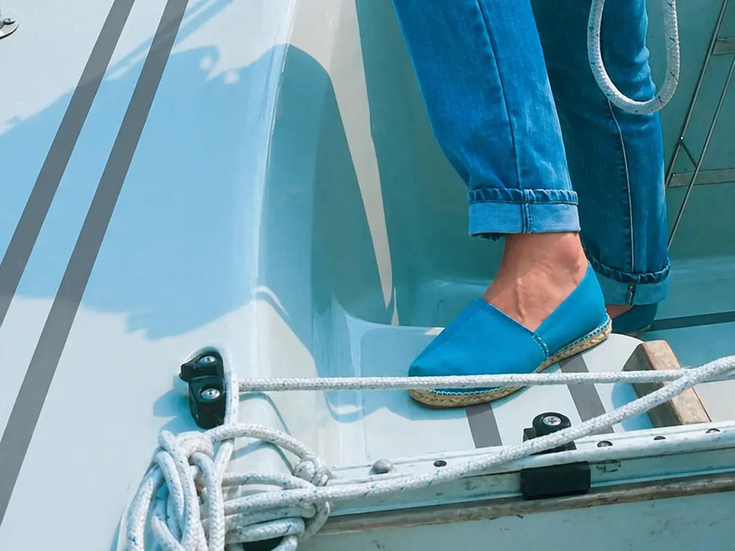 Grijze antislipstrips op een wit bootdek met touwen en een blauwe schoen, toegepast als subtiele veiligheidsmarkering voor grip aan boord.