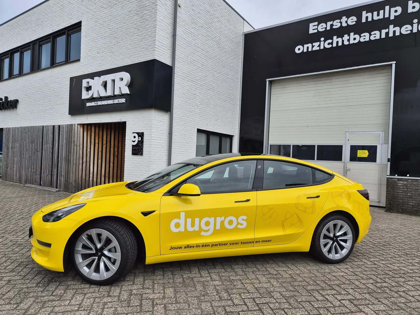 Side view of the yellow Dugros Tesla with a large white logo and subtle bag illustrations on the rear body panels.