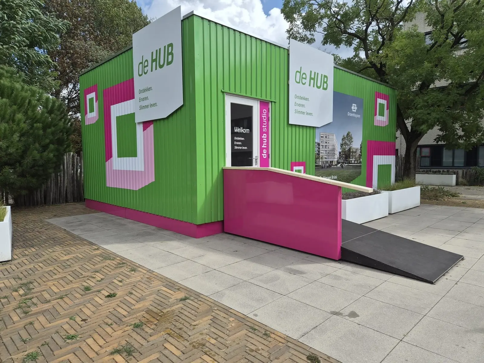 HUB Studio van Groenhuysen met groene bestickering, roze entree en witte informatiepanelen.