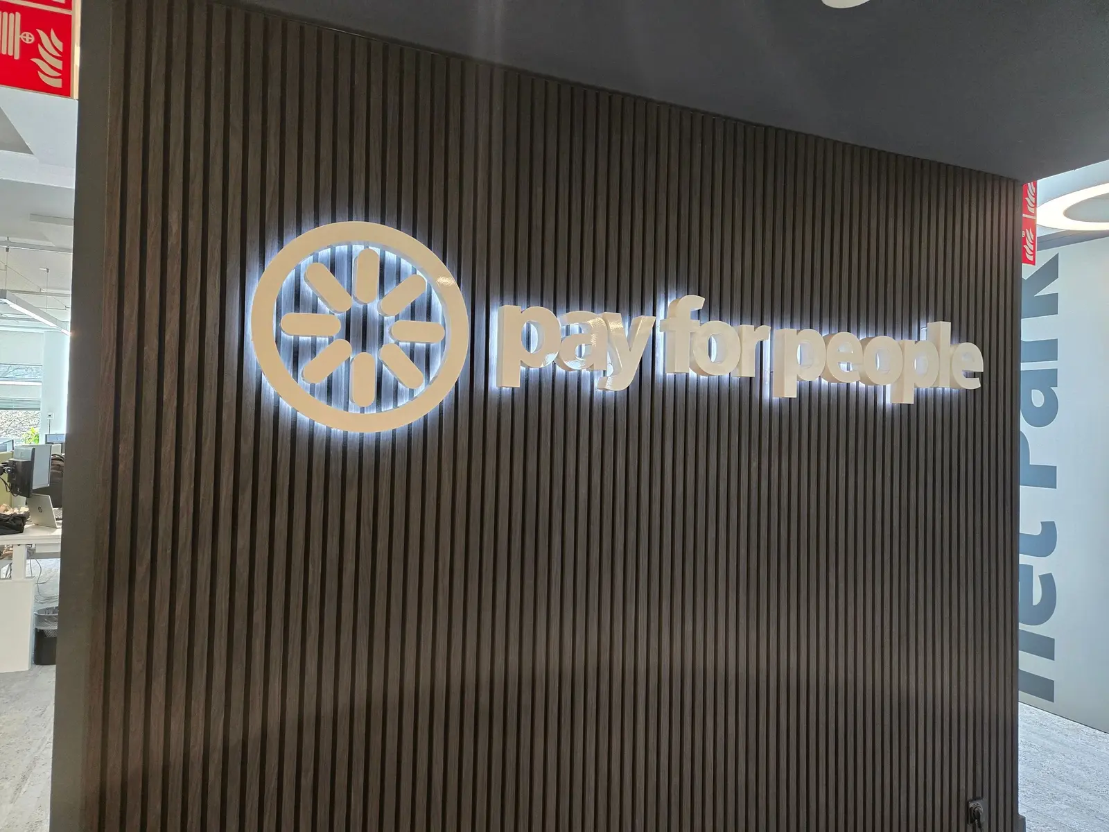 Witte PayforPeople-doosletters met lichtkrans op een donkere lattenwand in het kantoor.