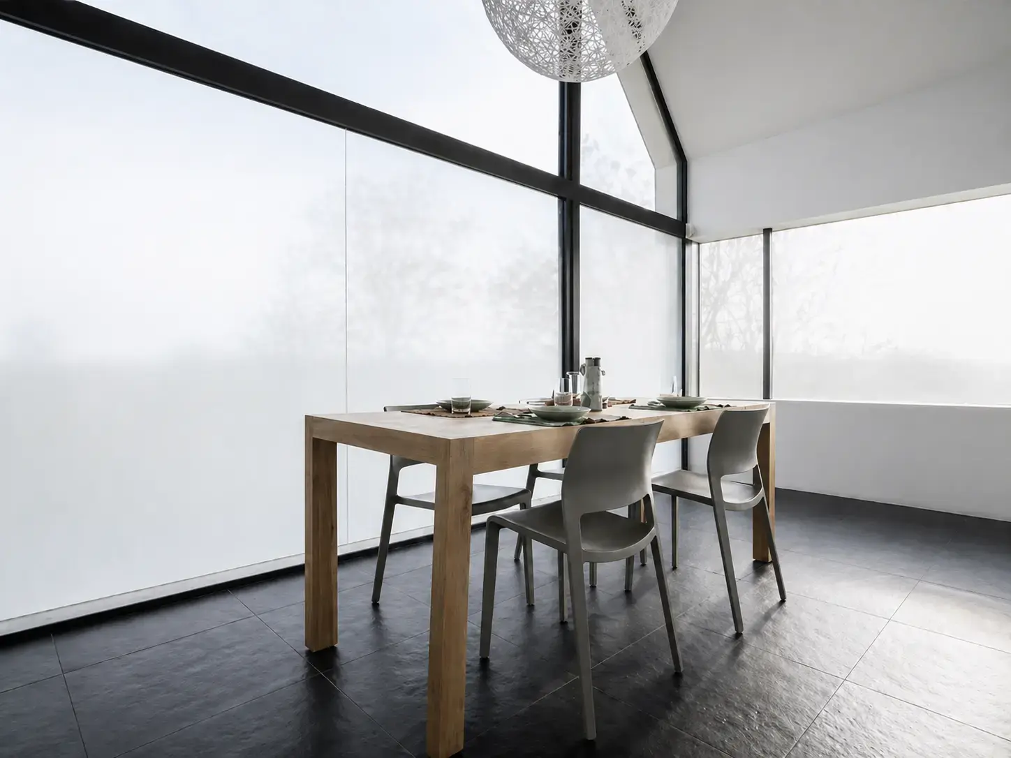 Matte privacyfolie op grote raampartijen in een moderne eetruimte met houten tafel en zwarte kozijnen.